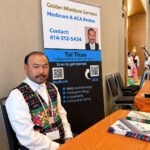 Tai Thao in traditional Hmong dress at the Golden Milestone Services Medicare and ACA information table during the Sheboygan Hmong New Year celebration